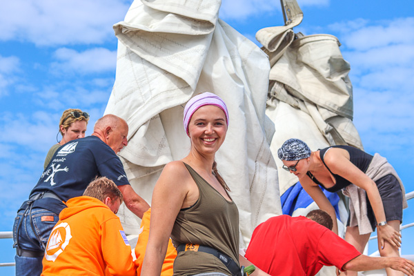 Meisje met hoofddoek om lacht met op de achtergrond de anderen die de zeilen hijsen
